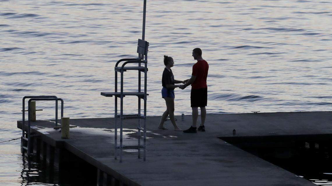 A couple holds hands while standing at the pier of the Wells College Boathouse along Cayuga Lake, Saturday, Aug. 11, 2018, in Aurora, N.Y. (AP Photo/Julio Cortez)