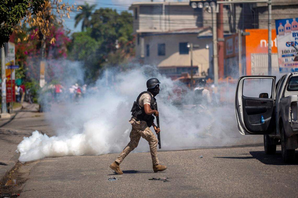 A police officer runs away from tear gas during a protest to demand the resignation of Haiti’s President Jovenel Moise in Port-au-Prince, Haiti, Wednesday, Feb. 10, 2021. Haiti has lurched into fresh political crisis amid allegations of a coup attempt and an escalating dispute over when the presidential term of Moise should end.