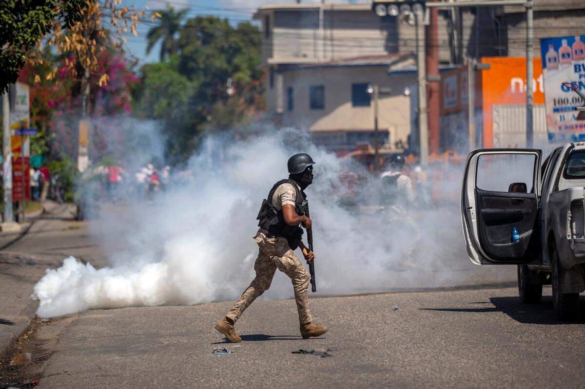A police officer runs away from tear gas during a protest to demand the resignation of Haiti’s President Jovenel Moise in Port-au-Prince, Haiti, Wednesday, Feb. 10, 2021. Haiti has lurched into fresh political crisis amid allegations of a coup attempt and an escalating dispute over when the presidential term of Moise should end.