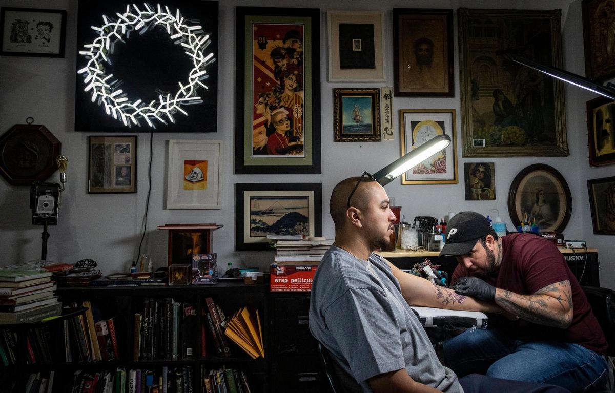 Javier Betancourt, right, works on a piece in his Ocho Placas tattoo shop, which he combined with his White Rose Coffee shop.