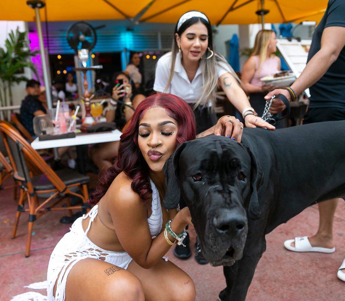 Lae’la Labeaud, a tourist from New Orleans, hugs Panther, a great dane, while visiting Miami Beach, Florida on Friday, March 25, 2022. City officials imposed a midnight curfew and forced stores to stop selling alcohol after 6 p.m. The restrictions were set in place after two shootings in Miami Beach the weekend before caused city officials to announce a “state of emergency.”