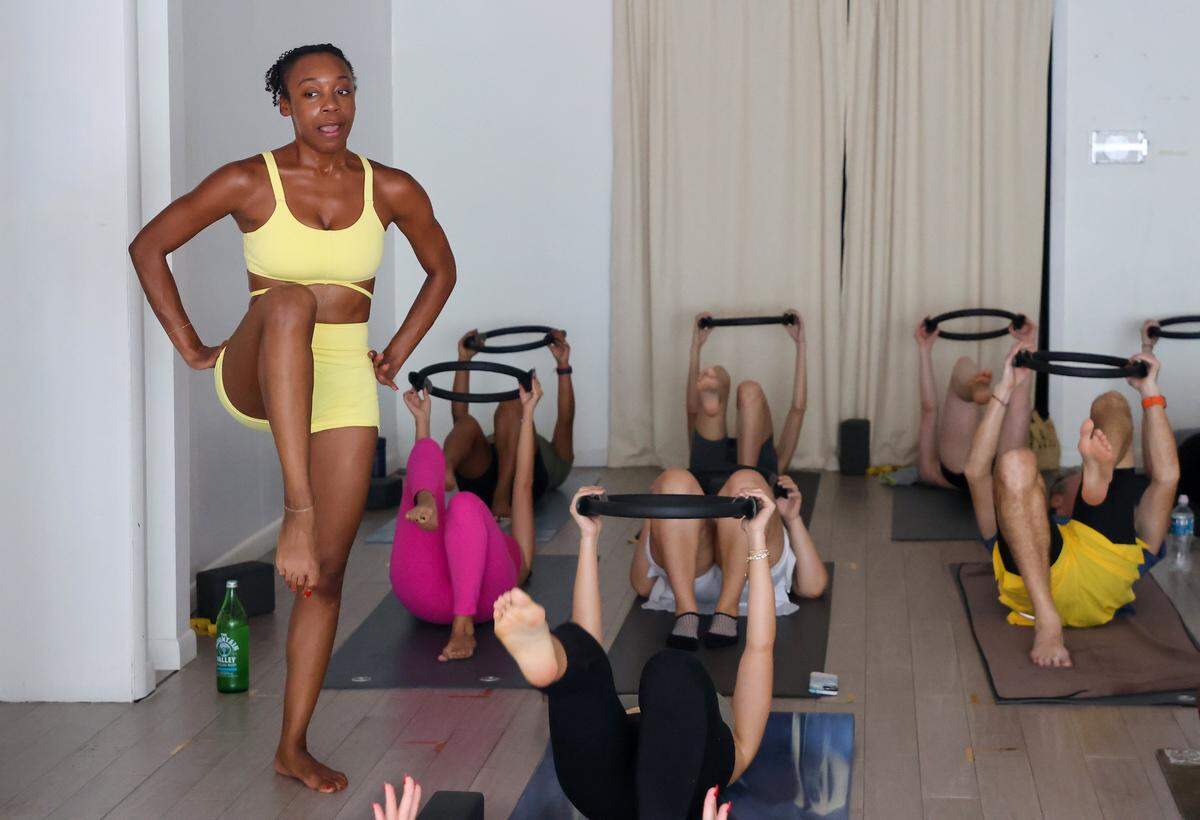 Navy vet and Pilates instructor Shay Williams encourages proper form as attendees lift their right legs while posing using a ring during yoga class at Hand Yoga in Miami Beach, Florida on Sunday, November 9, 2025.