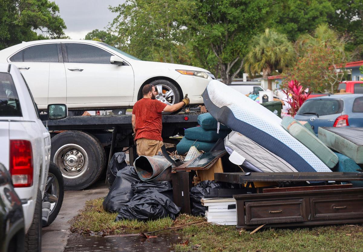 Neighbors discard damaged items in a pile on the street. A tow-truck operator gives a thumbs up as one of many damaged cars is towed away on Monday, April 17, 2023.