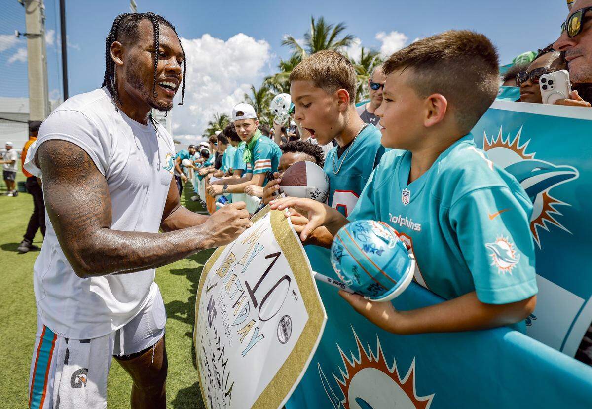 Miami Dolphins wide receiver Dee Eskridge, left, signs a happy birthday sign for AJ Spies, 10, at right, as his brother Damion Spies, 13, reacts after a joint practice against the Jacksonville Jaguars.