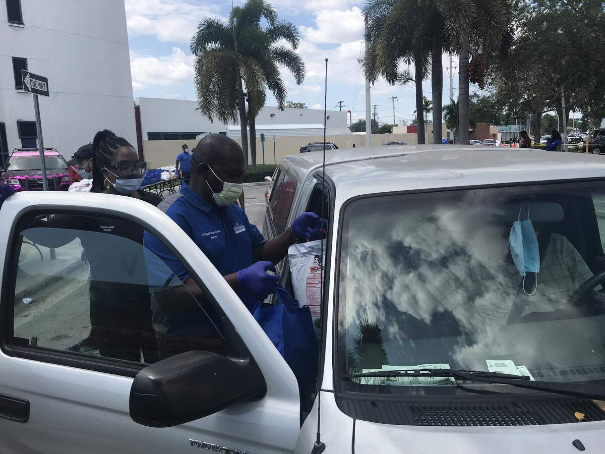 North Miami Mayor Philippe Bien Aime helps load a bag of pasta, beans, bread and other dry goods into a vehcile during the city’s food giveaway for North Miami residents on Friday, April 3, 2020.