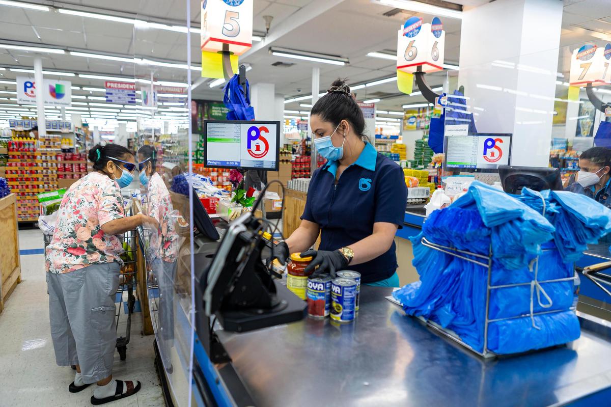 Mairelis Hernandez, 28, a cashier at Presidente Supermarket, works the register at a store in Allapattah, Florida on Monday, May 11, 2020.