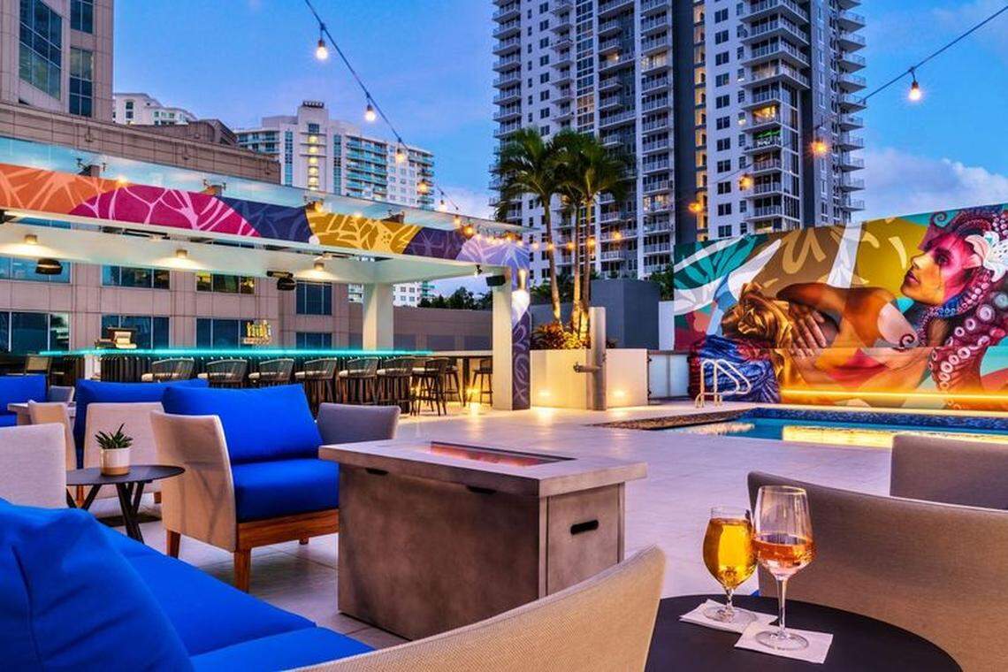 An open rooftop bar alongside a pool is decorated with hanging lights and bright wall art at ELEV8 in Fort Lauderdale. 