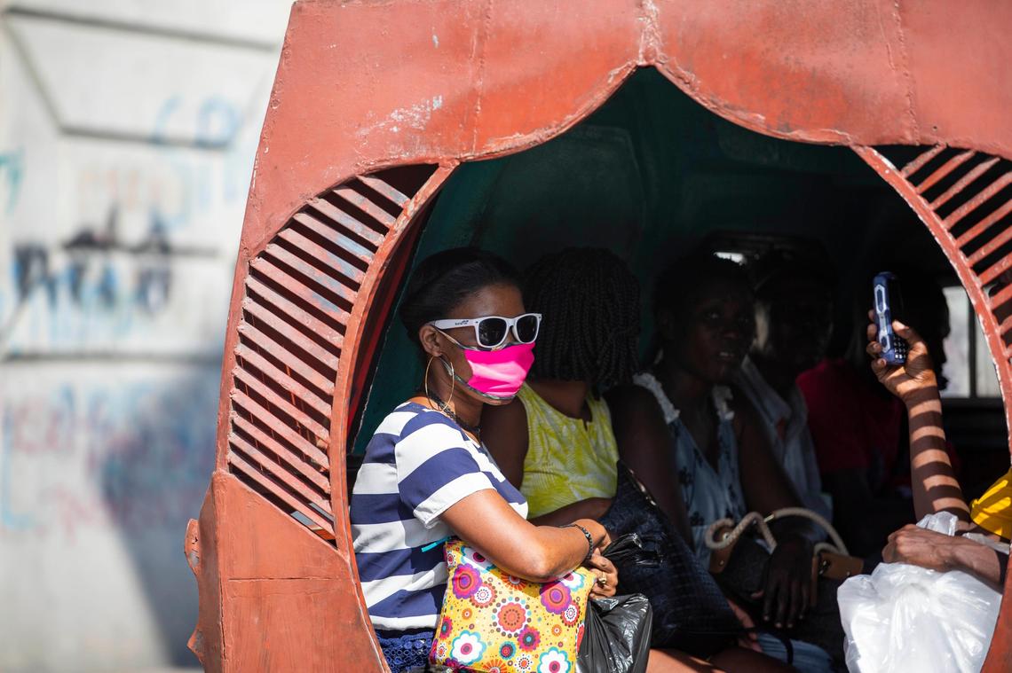 People sit in a Tap-tap while a passenger wears a mask to protect herself from the spread of the new coronavirus in Port-au-Prince, Haiti. Fear of insecurity has ridership on public buses down, transport unions say.