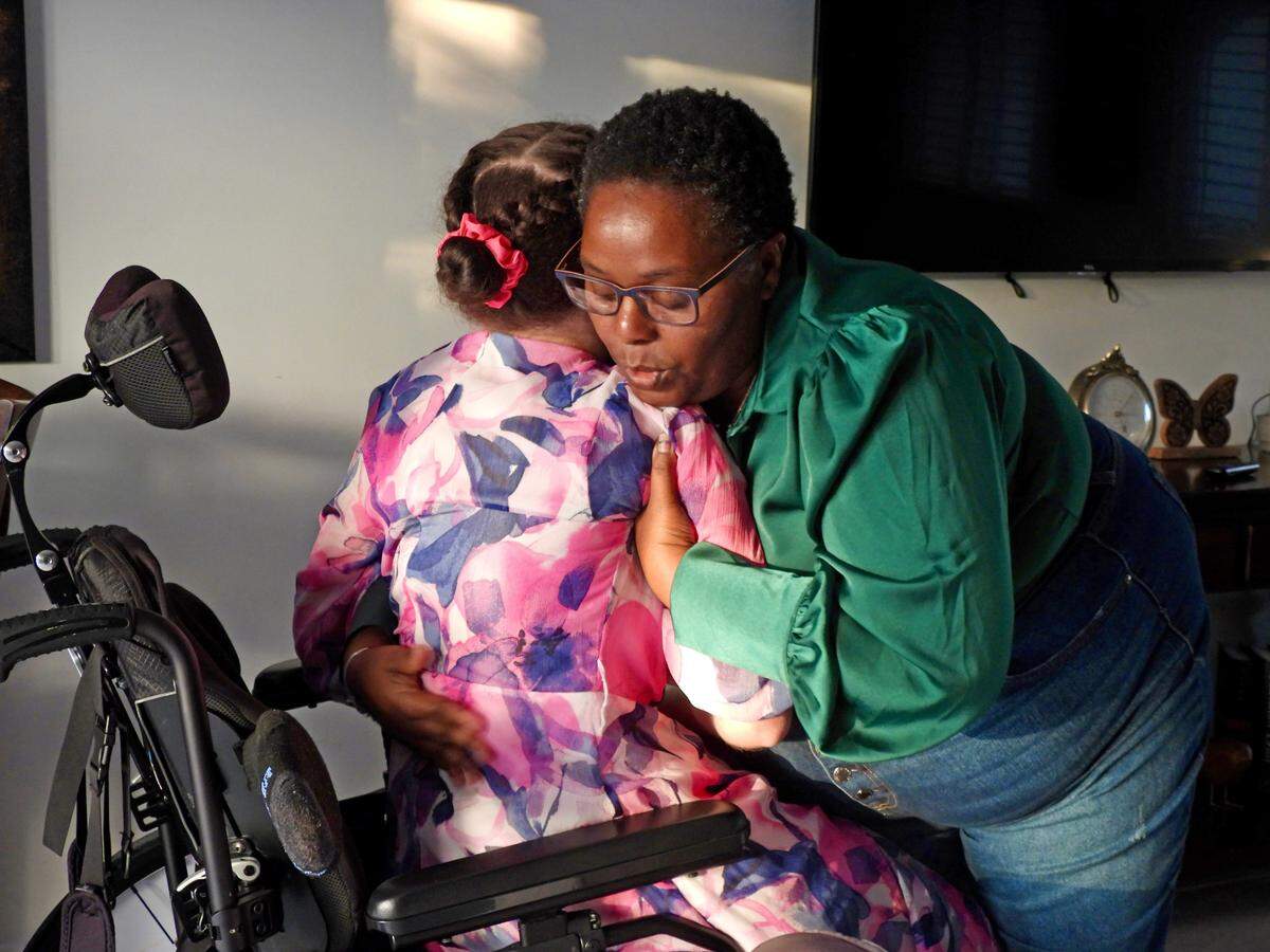 Marie “Michelle” Delva transfers Alexa Mitchell into a lounge chair in her group home.