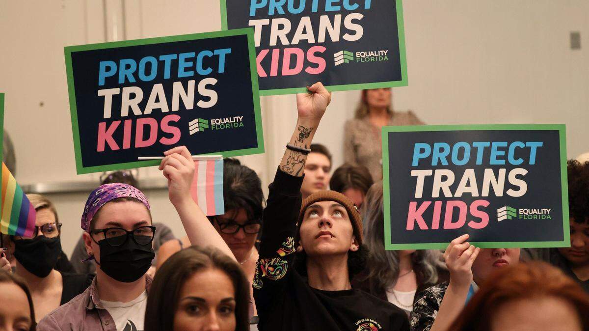 People hold signs during a joint board meeting of the Florida Board of Medicine and the Florida Board of Osteopathic Medicine, Friday, Nov. 4, 2022, in Lake Buena Vista, Fla., to establish new guidelines limiting gender-affirming care in Florida.