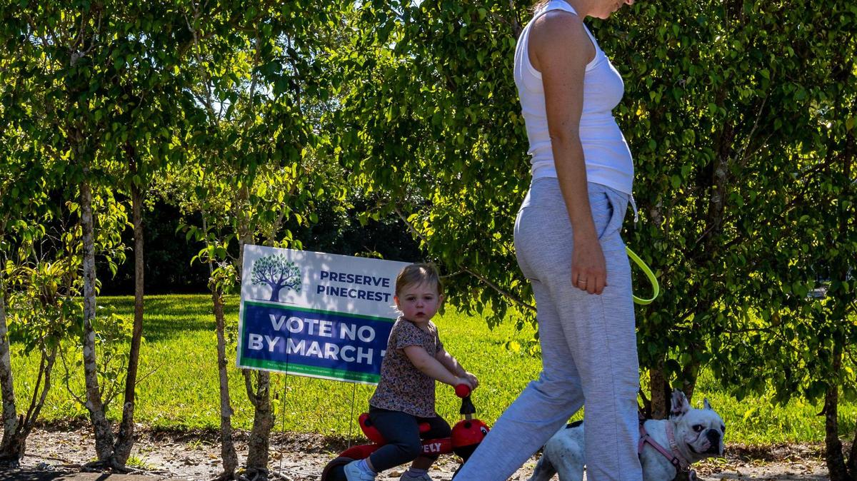 Pinecrest resident Corinne Bonner and her daughter Kiera and dog Piggy walk past a sign that reads ‘VOTE NO’ in front of a resident’s yard in Pinecrest, Florida, on Wednesday, March 1, 2023. Bonner said she already voted no on the new referendum.