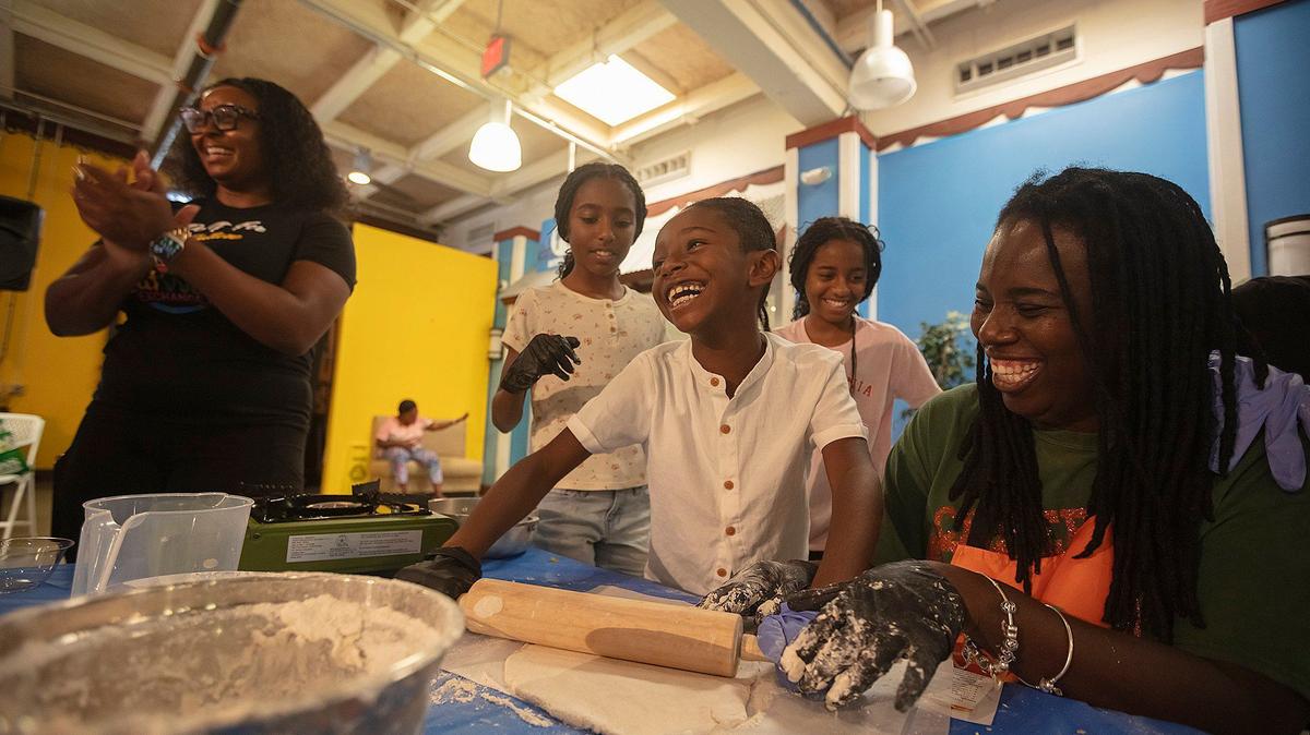 Marcellus Francis 7, laughs while rolling out dough. He is flanked by his twin sisters, Morgan Francis, 10, and Madison Francis, 10, as their mother Lavi Francis, right, looks on during the cooking class by Eatwell Exchange at the Little Haiti Cultural Complex in Miami, Saturday, Sept. 7, 2024. Standing on the left is Ashley Carter.