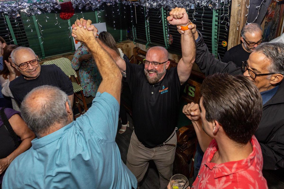 El comisionado electo Damián Pardo celebra con sus amigos Xavier Cortada, Adam Roberti y Jorge Mursuli mientras reacciona a la noticia de haber desbancado a la actual comisionada Sabina Covo, durante una fiesta de observación de la segunda vuelta electoral para el asiento de la comisión del Distrito 2 de Miami en Flanigan's, en Miami, Florida, el martes 21 de noviembre de 2023.