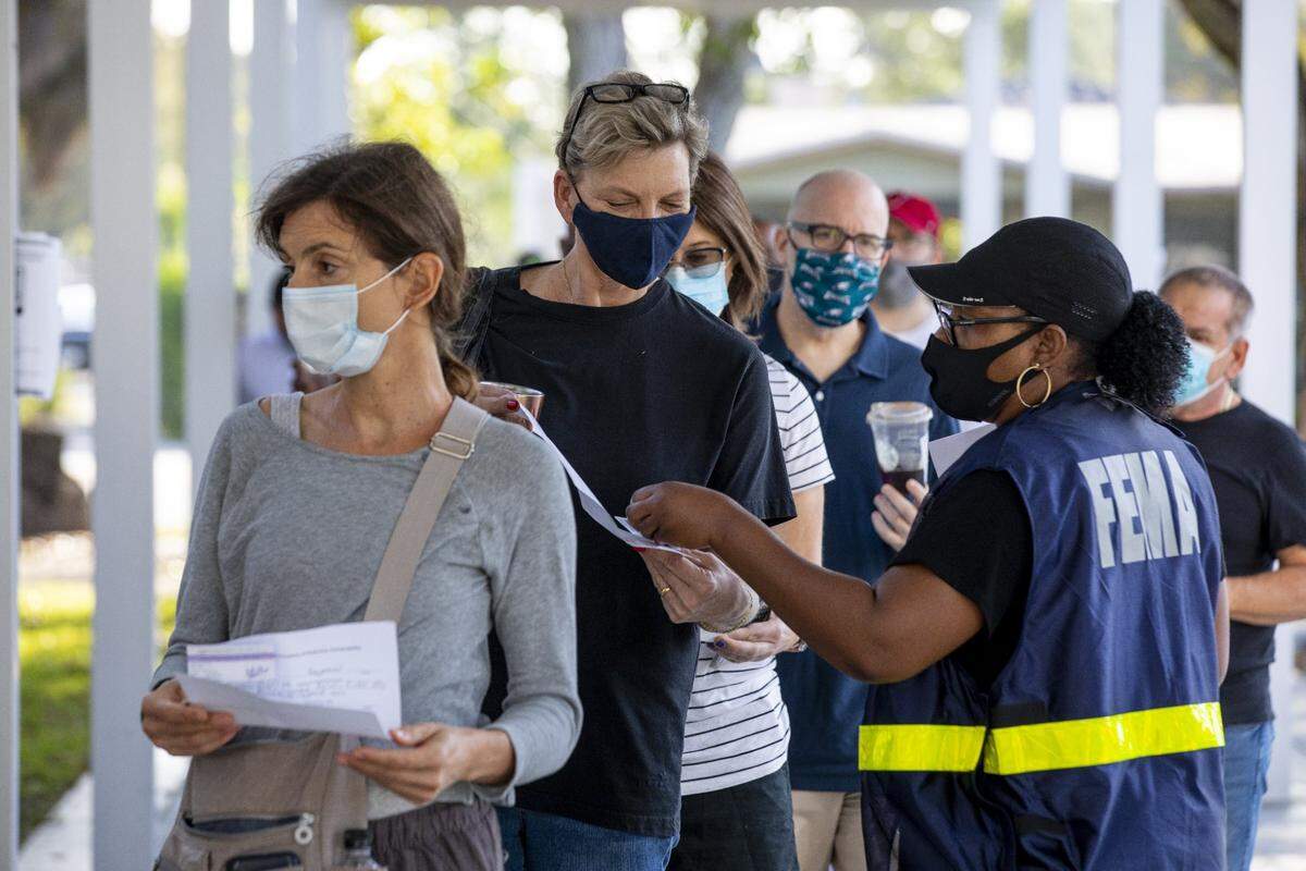 Un empleado de FEMA ayuda a la residente de Miami Heide Werthamer, de 56 años, mientras espera recibir una vacuna en el nuevo sitio satélite de la vacuna COVID-19 administrado por el estado y respaldado por FEMA dentro del Centro Juvenil Samuel K. Johnson en Charles Hadley Park en Liberty City, Florida, el viernes 19 de marzo de 2021.