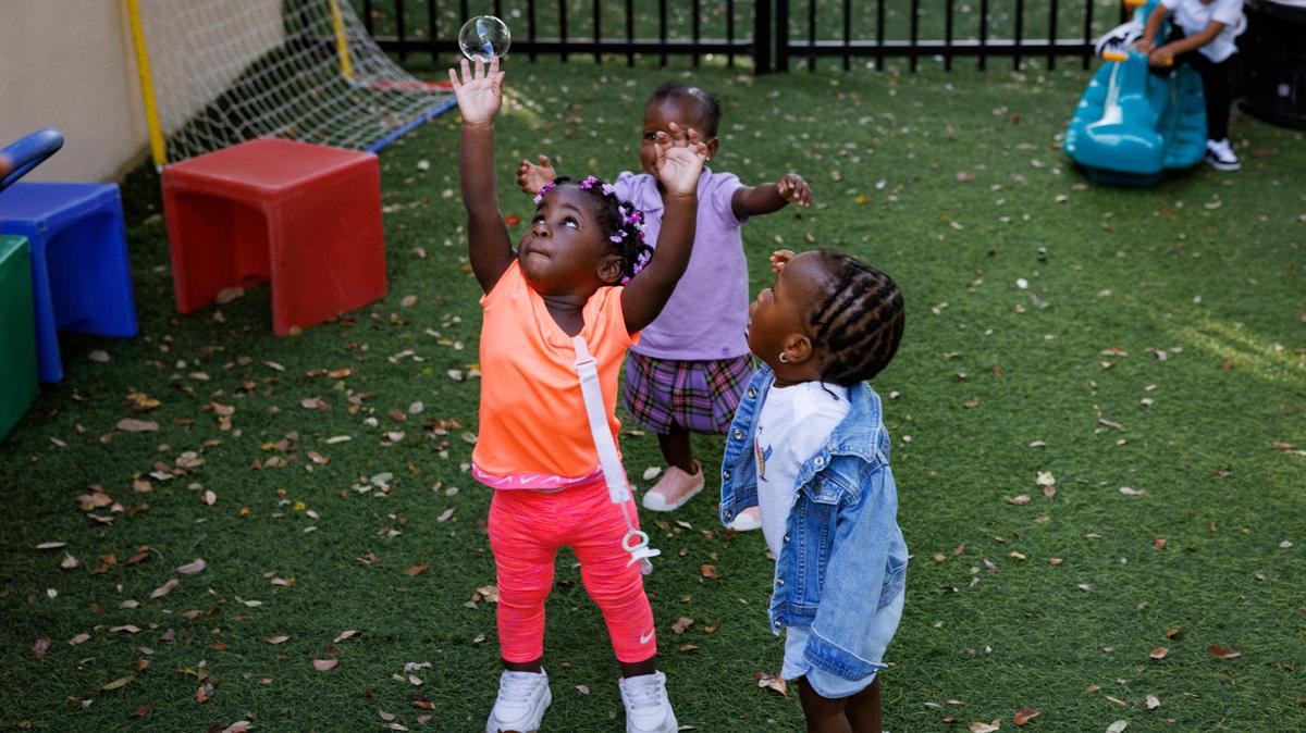 Cali, left, pops a bubble while playing with Treasure, right, and other 1-year-olds at the playground on Wednesday, Nov. 13, 2024, at Liberty Academy, a school and aftercare facility in Liberty City.