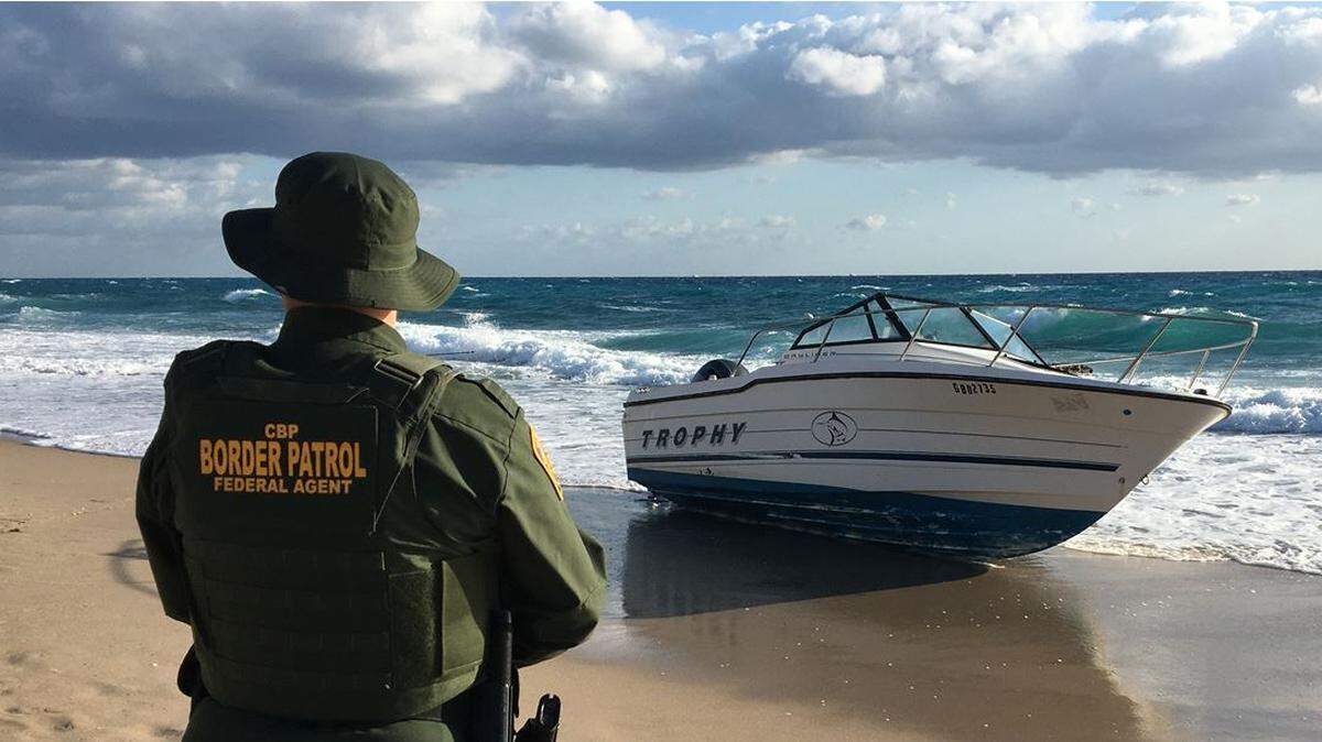 A U.S. Border Patrol agent stands guard by a Bayliner Trophy cabin cruiser that came ashore on Palm Beach Monday, March 2, 2020, carrying migrants and six packages of marijuana, federal authorities say.