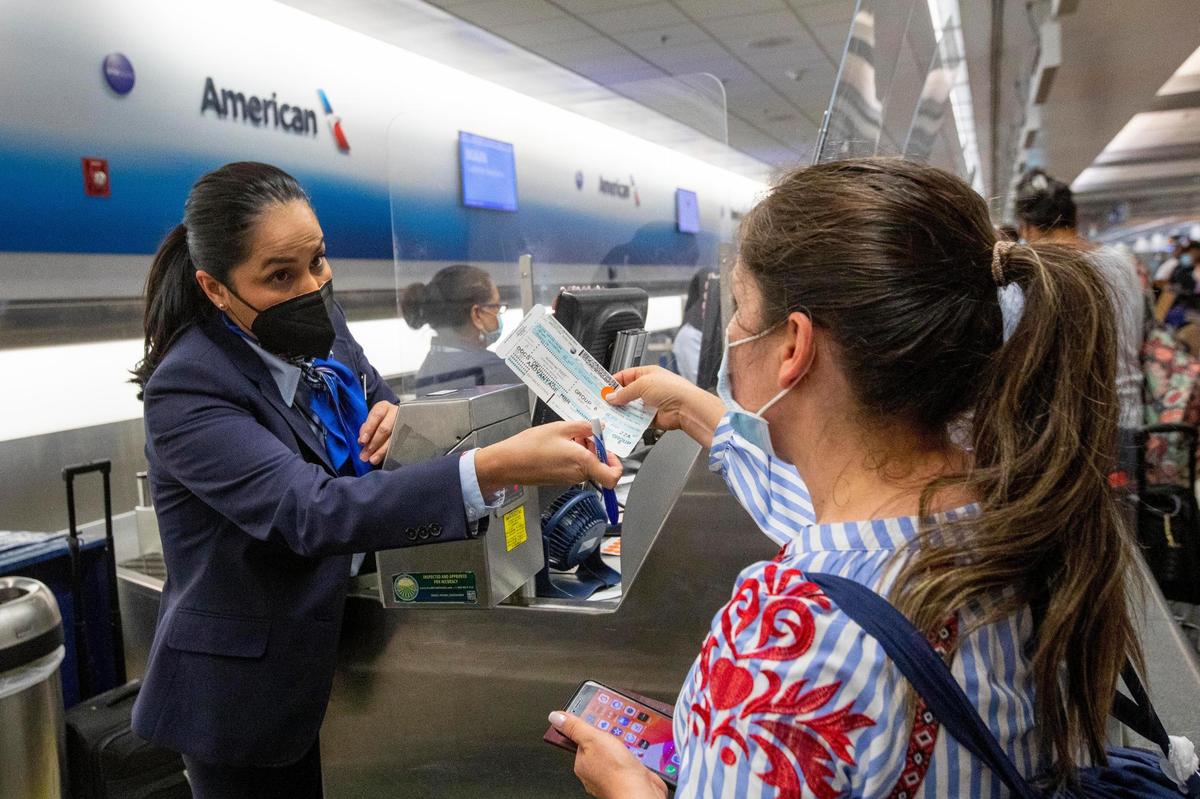 Una empleada de American Airlines entrega a una viajera su boleto de embarque tras usar 4  VeriFLY, una aplicación para teléfonos móvoles que permite a cargar la documentación que demuestra que la prueba de COVID ha sido negativa o que se ha vacunado, mientras se registra antes de su vuelo internacional en el Aeropuerto Internacional de Miami, el lunes 7 de junio de 2021.