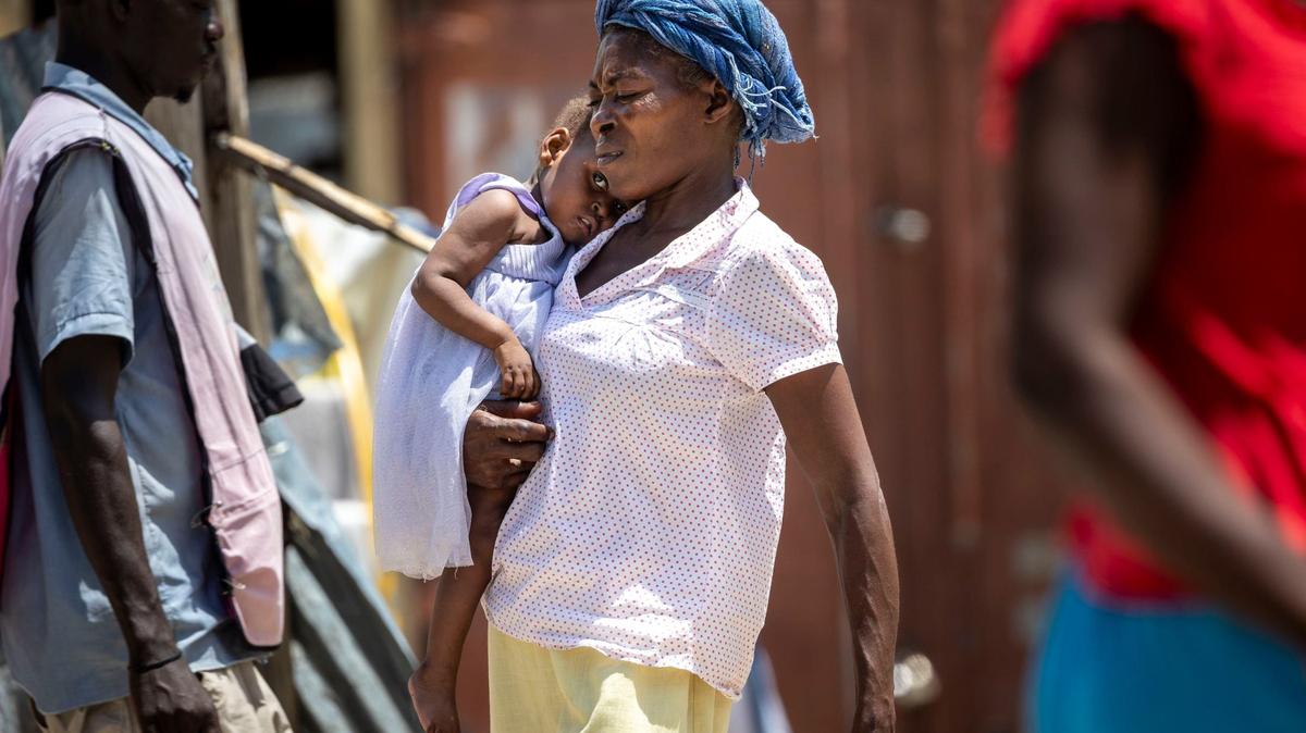 A woman carries a child across the school yard at Ecole National Joseph C. Bernard DeFreres displacement camp on August 27, 2024. Residents of areas in Port-au-Prince have been forced to take refuge in camps such as this rather than stay in gang occupied territories.