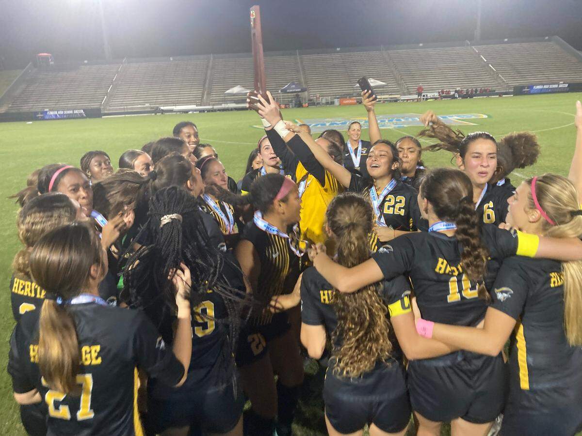 The American Heritage girls soccer team celebrates with the trophy Friday night after winning the Class 5A state championship match at Spec Martin Stadium in DeLand, Fla.