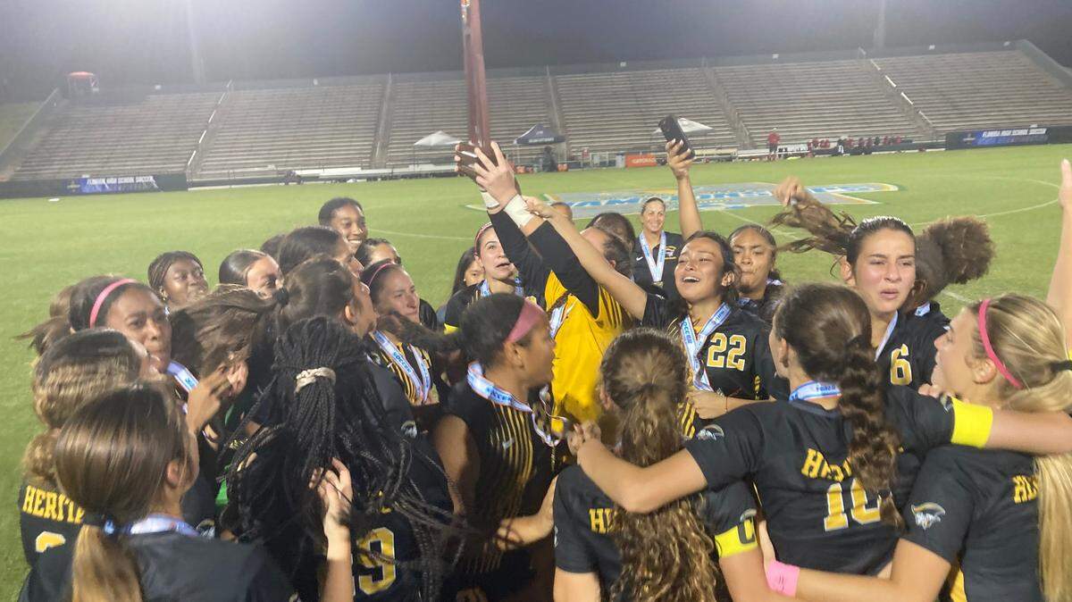 The American Heritage girls soccer team celebrates with the trophy Friday night after winning the Class 5A state championship match at Spec Martin Stadium in DeLand, Fla.