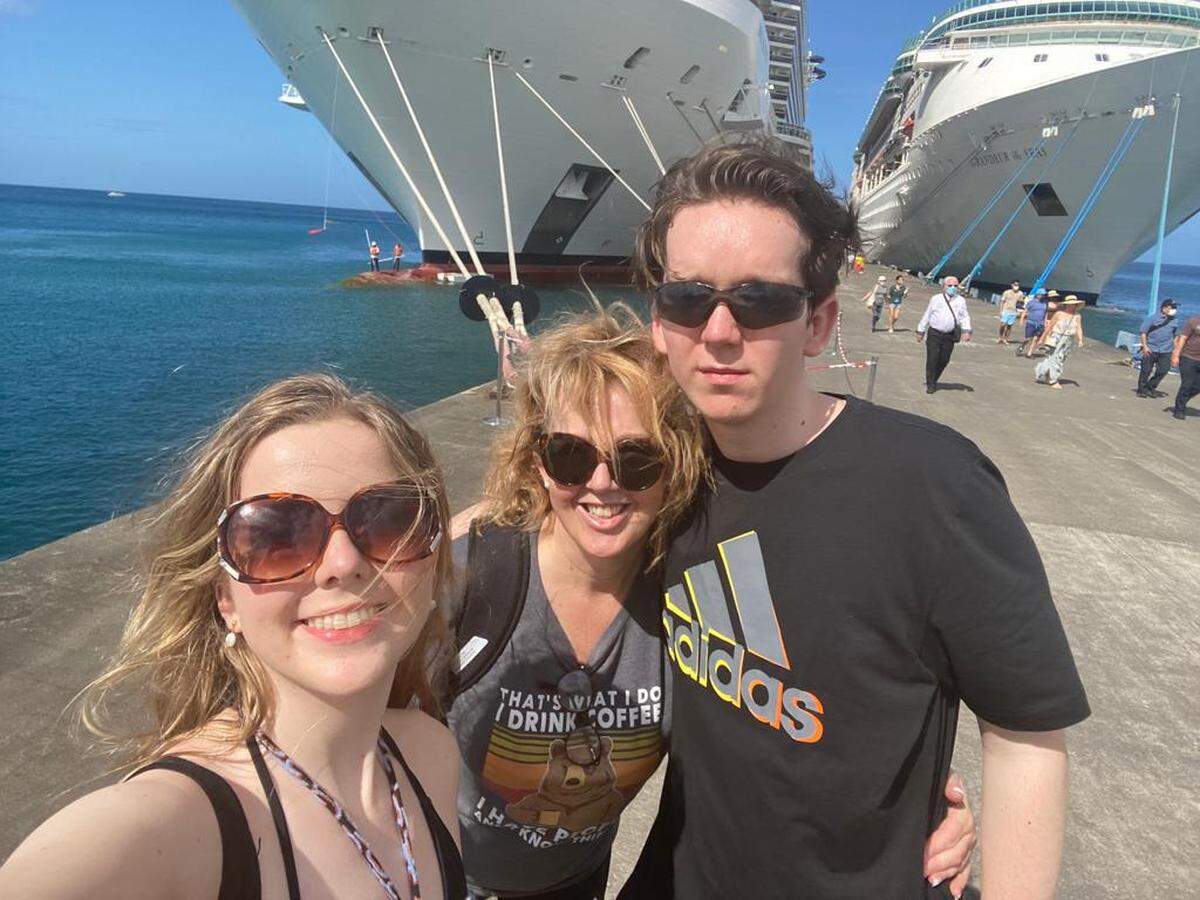 Laurie Browne (centro), su hija Lara (izquierda) y su hijo Luke (derecha) posando junto al crucero MSC Seaview (izquierda). Browne y su hija dieron positivo en la prueba de COVID-19, mientras viajaban en el barco que partió de Barbados el 21 de diciembre.