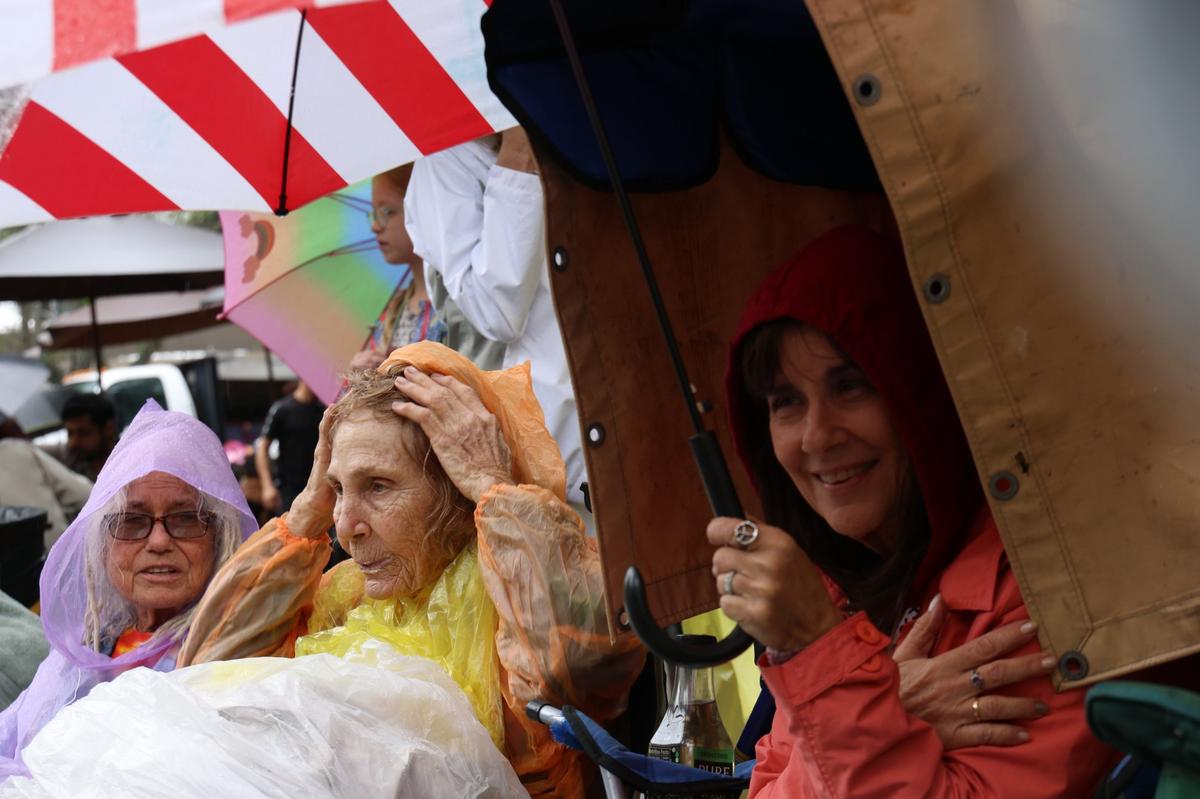 Parade fans - Silver Lanz, left, Linda Blissberger, and Barbara Khury, right, are all ready for the rain as they sit on the parade route. It was singing, dancing, and parading in the rain as Coconut Grove held its annual satirical parade on Sunday, January 7, 2023 in Miami, Florida.
