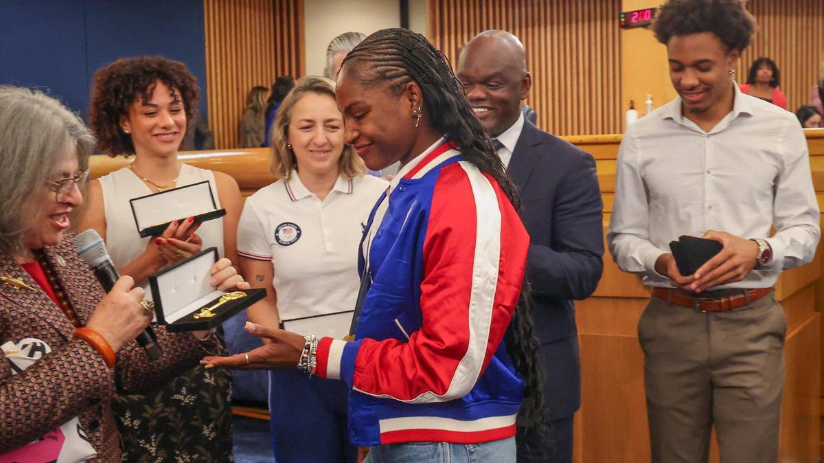 Twanisha “Tee Tee” Terry, who won gold in women’s track and field in the 4x100m relay, receives her key to the County from Mayor Daniella Levine Cava, right, as other outstanding Olympians from Miami-Dade looked on and were honored with keys to the County, in recognition of their remarkable achievements and contributions to sports on Wednesday, September 4, 2024, inside Miami-Dade Commission chamber at the Stephen P. Clark Center in Miami, Florida. Left to right: Mayor Daniella Levine Cava, Daniella Ramirez (artistic swimming), Sarah Newberry Moore (sailing), Commissioner Kionne McGhee, and Russell Robinson (track and field), right.