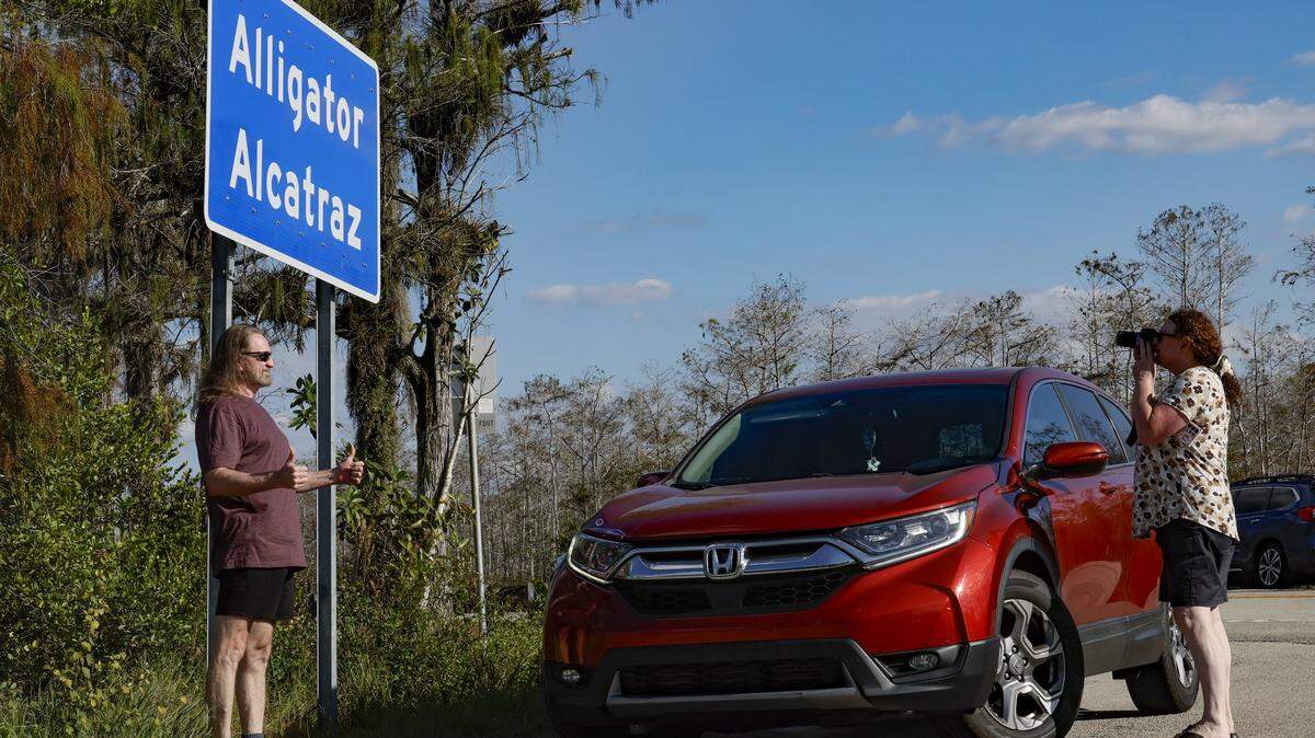 Flashing a thumbs up and posing for photographs is a man standing underneath the sign at the front entrance to Alligator Alcatraz, an immigration detention facility along Tamiami Trail, and located at Dade-Collier Training and Transition Airport inside Big Cypress National Preserve in Ochopee, Florida on Wednesday, November 19, 2025.