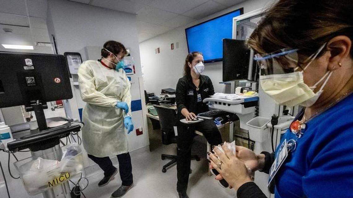 Nurse Alix Zacharski, right, sanitizes her hands as other doctors and nurses care for a patient in the Medical Intensive Care Unit for COVID-19 patients at Jackson Memorial Hospital in July 2021.