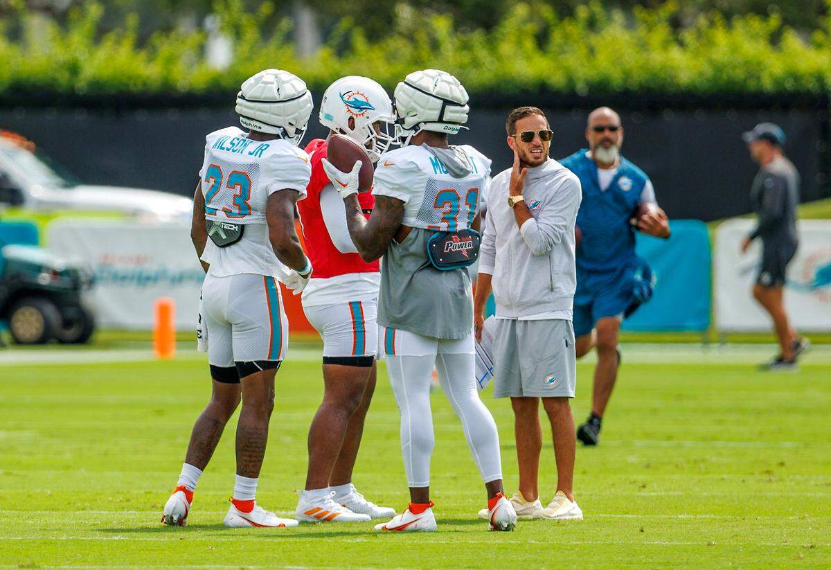 Miami Dolphins head coach Mike McDaniel talk with Dolphins quarterback Tua Tagovailoa (1) talks with Dolphins running backs Raheem Mostert (31) and Jeff Wilson Jr. (23) during NFL football training camp at Baptist Health Training Complex in Hard Rock Stadium on Thursday, August 3, 2023 in Miami Gardens, Florida.