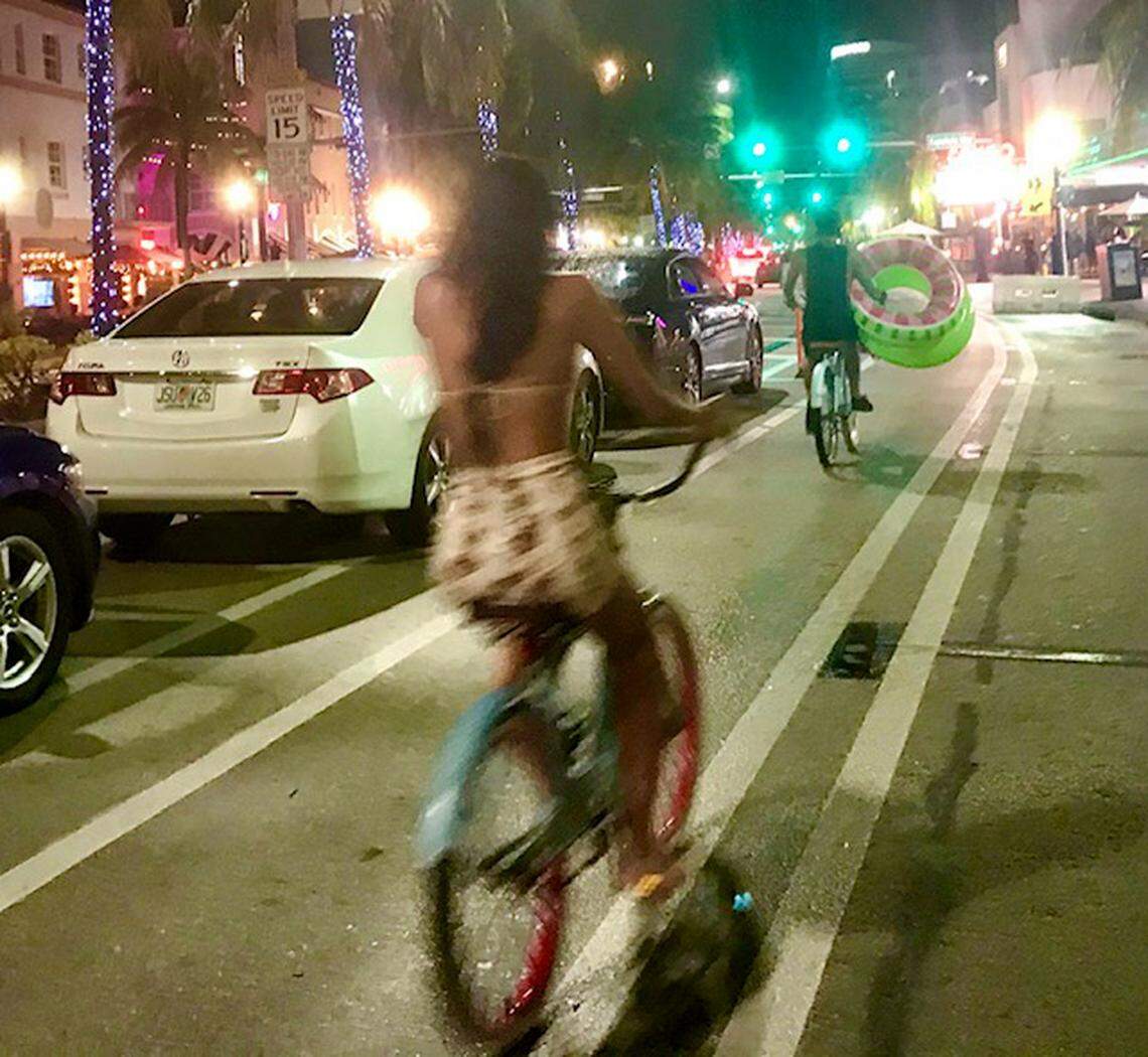 Two cyclists -- including one carrying innertubes from the beach -- ride in the new parking-protected bike lane on Washington Avenue in Miami Beach.