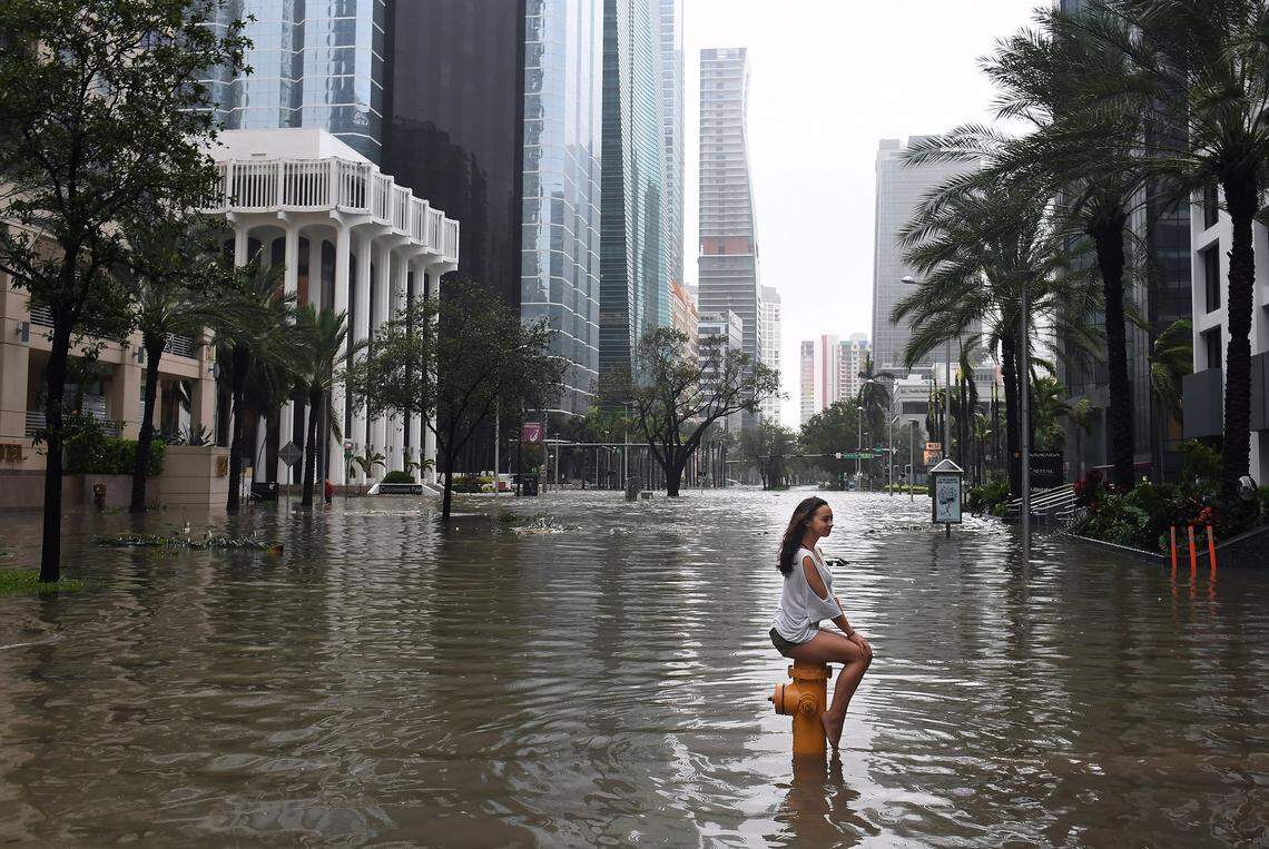 A new government report from a team of scientists warns that rising sea levels, particularly in Florida, mean greater damage from storm surges during hurricanes such as Hurricanes Michael and Irma. In this photo, Mia Herman perches atop a fire hydrant after Hurricane Irma flooded Brickell Avenue.