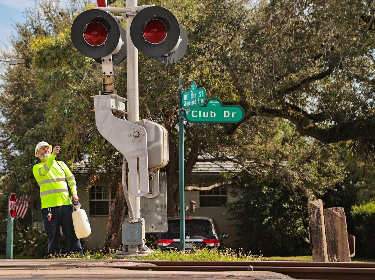 A signal support crew member sprays a signal light along the Brightline train corridor at the intersection of Northeast 96th Street and Club Drive in Miami Shores on Friday, Jan. 7, 2022.
