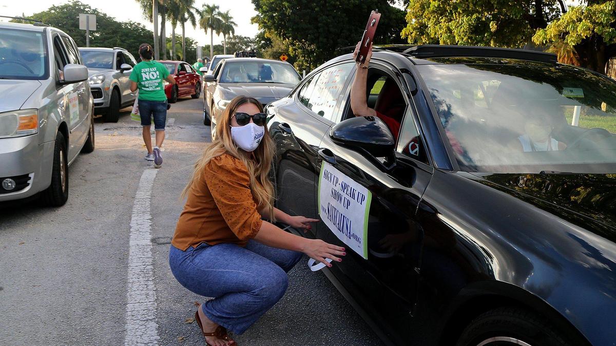Vanessa Vázquez coloca un poster en al auto de Caridad Vázquez mientras vecinos del vecindario Calusa en Kendall se preparan para comenzar una manifestación de “Save Calusa” como parte de una campaña para evitar el desarrollo de los terrenos del antiguo campo de golf para convertirlo en una subdivisión de 550 viviendas