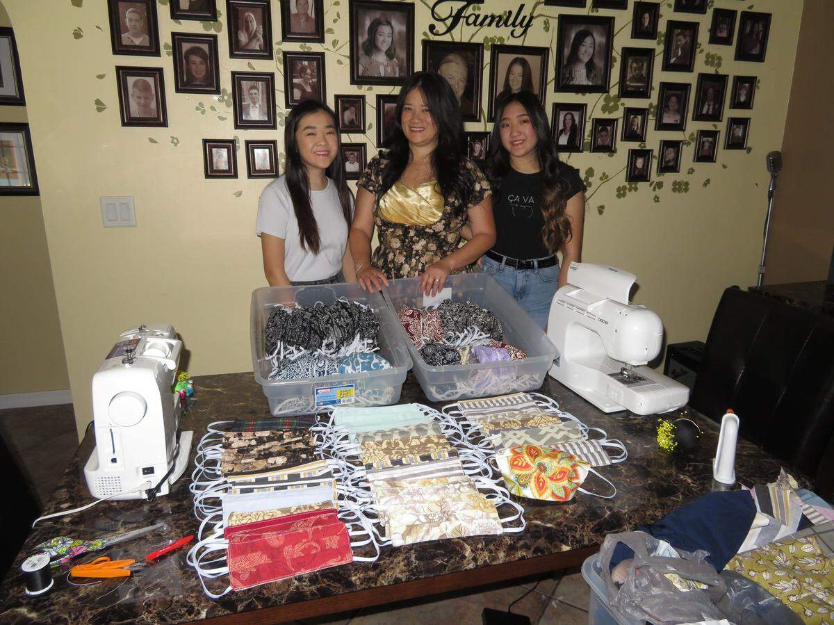 Miami Dade College student Olivia McAteer stands with her mother and sister beside some of the nearly 300 masks they have sewn at their Fort Myers home. The three have donated nearly 200 to workers in need and are now selling them to the general public to cover costs.