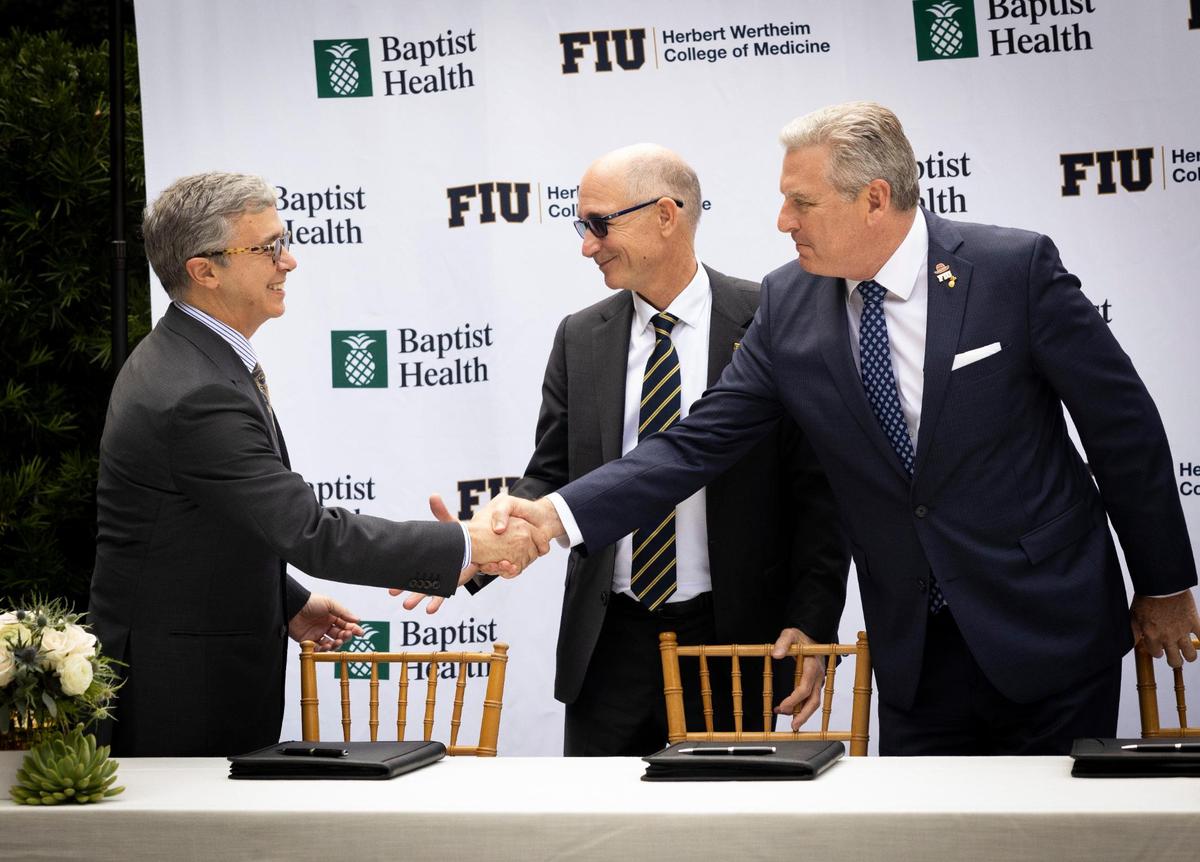 Juan Cendan, Dean of the Herbert Wertheim College of Medicine at FIU, left; Kenneth Jessell, FIU president, center; and Bo Boulenger, CEO of Baptist Health South Florida, shake hands during a signing ceremony for the clinical and academic partnership between Baptist Health and Florida International University on Tuesday, Nov. 28, 2023, at Baptist Health Miami Cancer Institute.