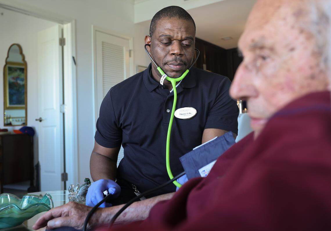 Medical responder Thievery Felix, left, takes the blood pressure of resident Gene Smolar, 93, right, on Thursday, Jan. 29, 2026, at Sinai Residences in Boca Raton, Florida.  Felix is one of dozens of Haitian workers at the retirement community. 
