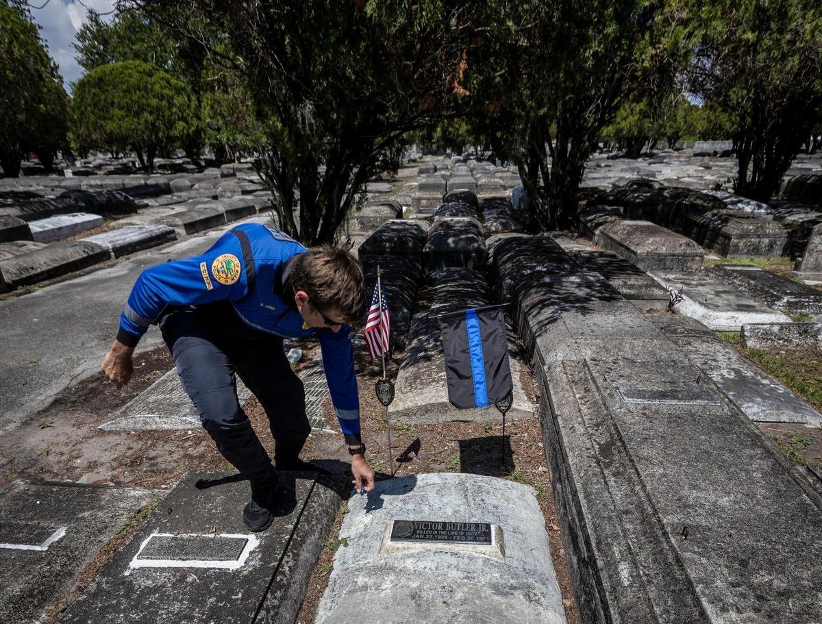 Miami, Florida, May 7 2021 - Commander Dan Kerr pics up debris scattered around the grave of officer Victor Butler who was killed in the line of duty in 1971. Officer Butler’s grave is Evergreen Memorial Park in Allapatah.