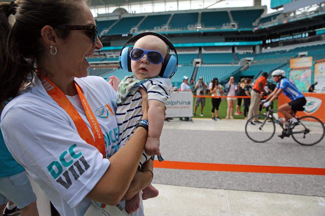 Pam Granoff holds 4-and-a-half month old Hayden Storm Simon who is all geared up to greet cyclists as they make their way into Hard Rock Stadium after completing their 100 mile ride for charity in this Feb. 10, 2018, file photo from the 8th Dolphins Cancer Challenge at Hard Rock Stadium.