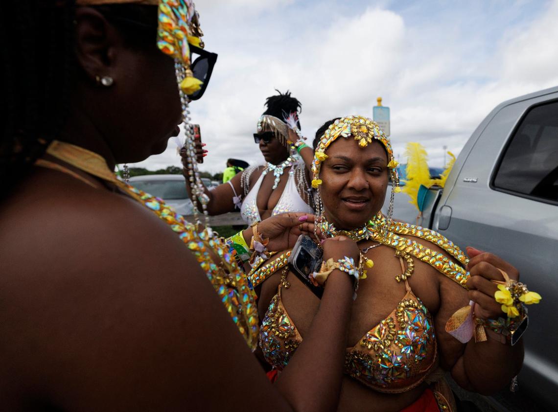 Nell, left, ties Marjorie’s costume, right, while their friend Niesha takes a selfie before the Parade of Bands in the parking lot at Miami Carnival on Sunday, Oct. 13, 2024, at Miami-Dade County Fair Expo.