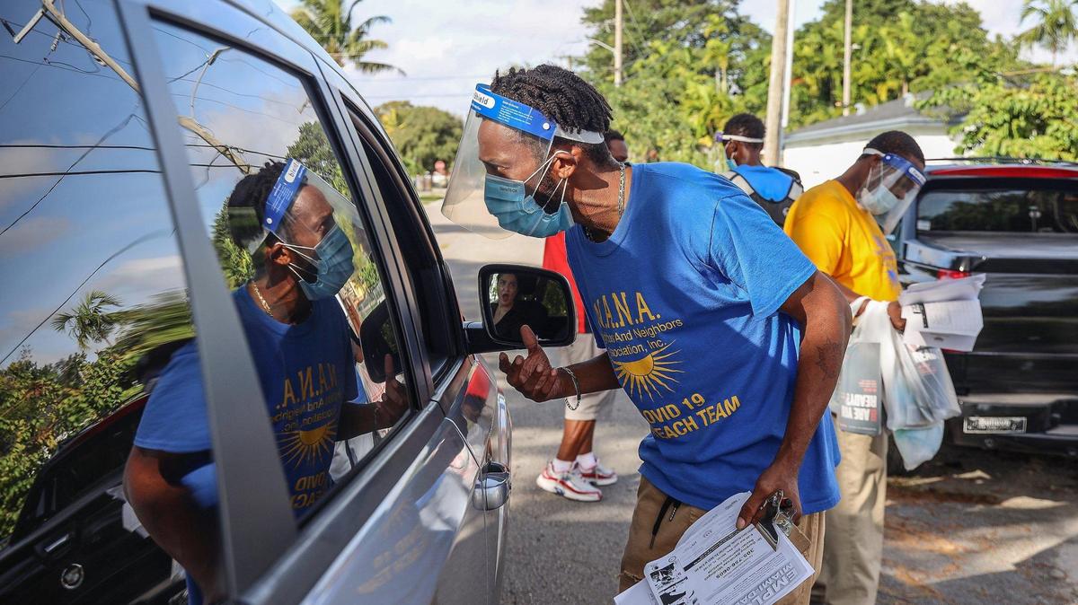On Wednesday, December 16, 2020 Calvin Wyche, 35, center, speaks to a resident while walking through Miami’s Brownsville neighbor handing out employment and COVID-19 information in Miami’s Brownville neighborhood. Members of the Neighbors And Neighbors Association’s (N.A.N.A.) COVID 19 Outreach Team talked to motorists, homeowners, and other residents as they spread the word about COVID-19 in the areas hardest hit by the virus. The three-man group handed out PPE as well as a survey that asks residents about how COVID has affected them. While not explicitly asking about the vaccine, many have heard hesitancy, specifically from Black and brown residents.