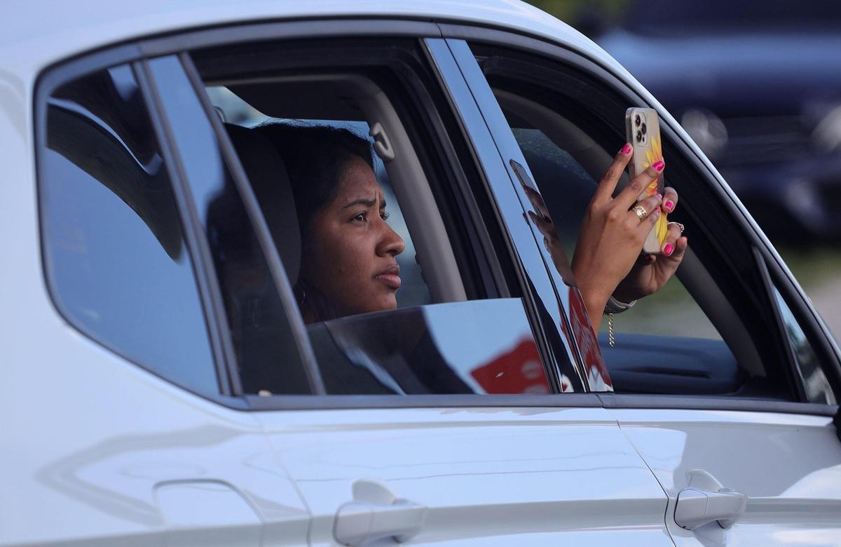 Shopper Alexandra Reyes, 23, uses her cellphone to record as Miami-Dade firefighters battled a large fire at flea market in Miami, Florida, on Thursday, July 7, 2022.