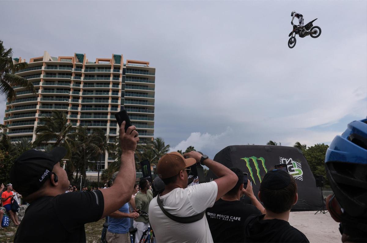 Brody Wilson, 36, takes to the air as the crowd is locked with eyes, cameras, and cellphones. On Sunday, May 29, 2022 motorcycle acrobatics met military precision in South Beach Sunday, as an Air Force honor guard performed drills on the sand as professional motorcross drivers jump their bikes in Lummus Park in South Beach.