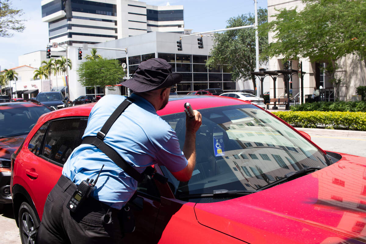 A Coral Gables parking enforcement officer checks to see if the displayed disability parking permit on a car parked on Miracle Mile is legitimate.