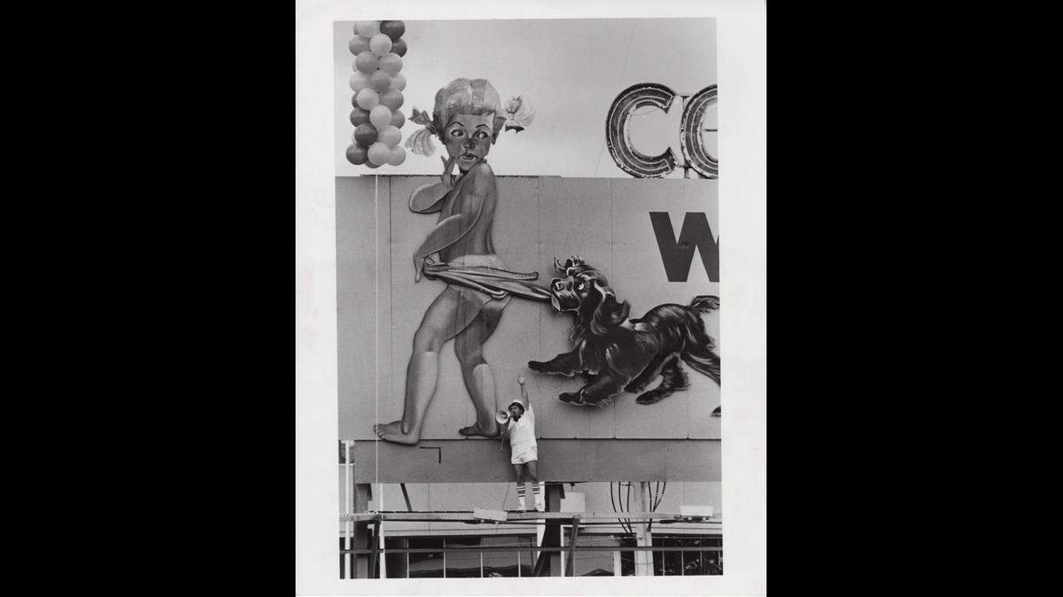 DJ Don Cox broadcasts from the Coppertone billboard on the Golden Glades Interchange in North Miami-Dade as part of a Power 96 radio stunt on Aug. 4, 1986 in this file photo. Cox got hit on the head by the dog’s paws. After seven stitches he was back on the air.