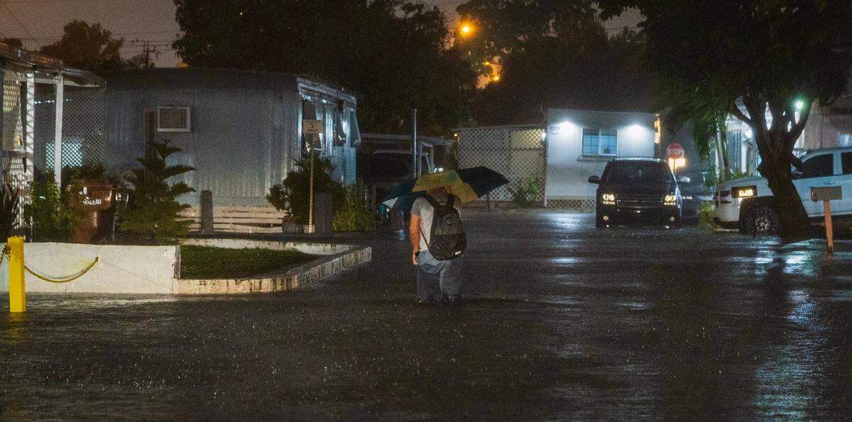 A man walks through a flooded street at the Strawberry Village Trailer Park located at West 29th Street and 16th Avenue in Hialeah as torrential downpours inundate South Florida due to a disturbance off Florida’s coast on Wednesday, November 15, 2023.