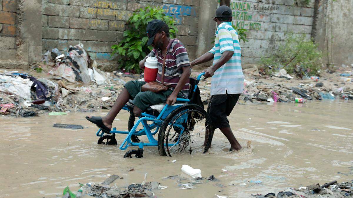 A man in a wheelchair is helped to make his way through a flooded street after a heavy rain, in Port-au-Prince, Haiti, Saturday, June 3, 2023.