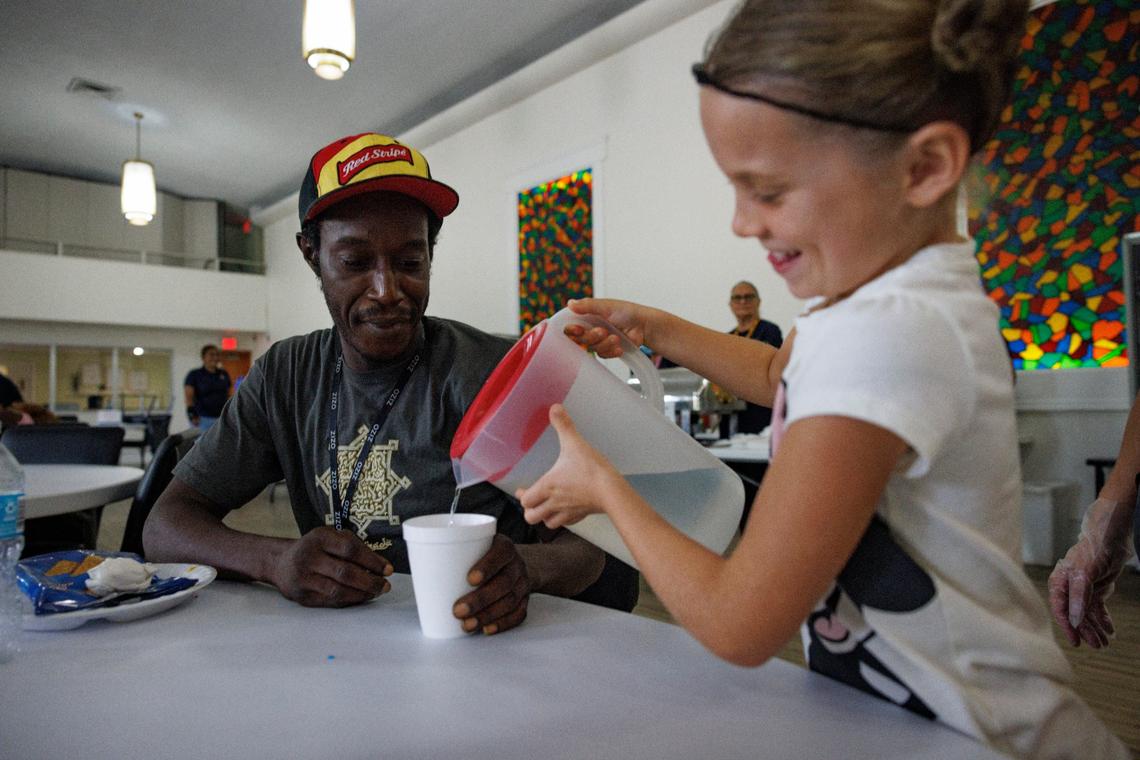 Celine Adams, 8, right, fills up Ken’s water cup during lunch time on Thursday, Sept. 5, 2024, at HOPE South Florida in Fort Lauderdale. Adams and her siblings take a break from homeschooling once a week to serve lunch to the community.