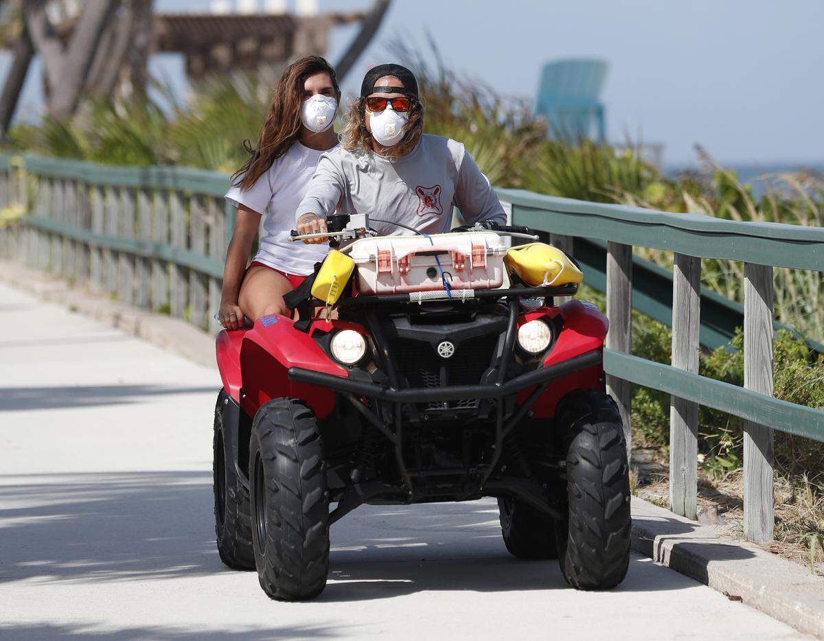 Palm Beach County Ocean Rescue workers wear masks as they ride an all terrain vehicle along Lake Worth Beach on Tuesday.