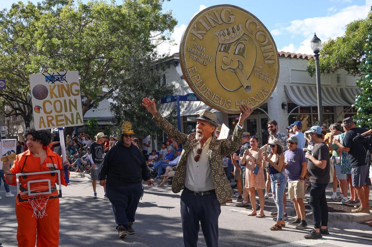 Buzz Fleischan, center, makes his pitch for “King Coin”’ a riff on the FTX debacle, as he tries to con parade attendees on purchasing the worthless digital currency.